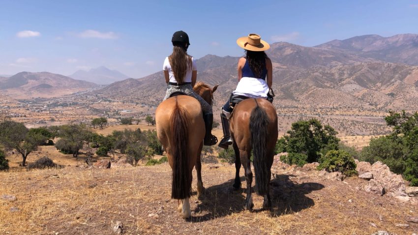 Two Women Riding Horses and facing the mountains in the Andes, Chile.